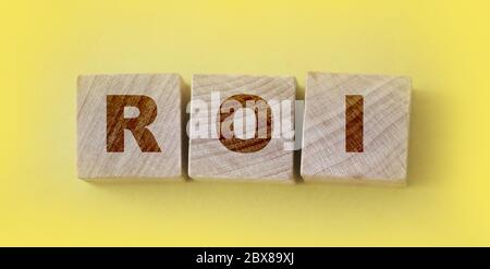 Acronym ROI Return on Investment. Wooden small cubes with letters isolated on yellow background. Business Concept image Stock Photo