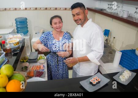 happy Asian couple cooking together -  home kitchen lifestyle portrait of Chinese cheerful and sweet husband and wife making delicious traditional Jap Stock Photo