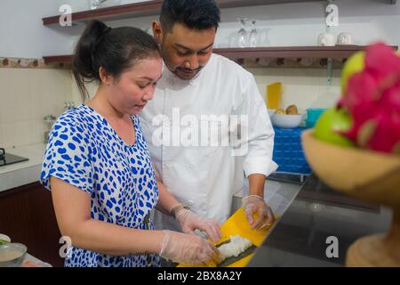 happy Asian couple cooking together -  home kitchen lifestyle portrait of Chinese cheerful and sweet husband and wife making delicious traditional Jap Stock Photo