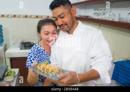 happy Asian couple cooking together -  home kitchen lifestyle portrait of Chinese cheerful and sweet husband and wife making delicious traditional Jap Stock Photo
