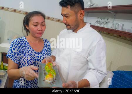 happy Asian couple cooking together -  home kitchen lifestyle portrait of Chinese cheerful and sweet husband and wife making delicious traditional Jap Stock Photo