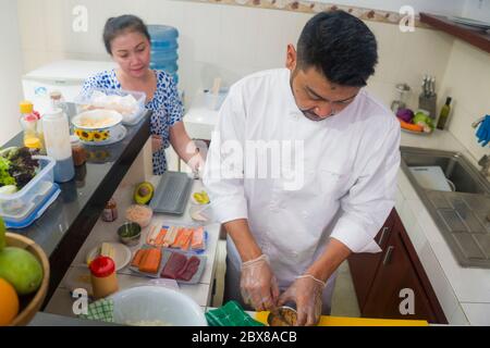 happy Asian couple cooking together -  home kitchen lifestyle portrait of Chinese cheerful and sweet husband and wife making delicious traditional Jap Stock Photo