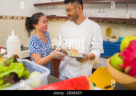 happy Asian couple cooking together -  home kitchen lifestyle portrait of Chinese cheerful and sweet husband and wife making delicious traditional Jap Stock Photo
