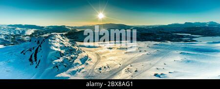 Scenic Aerial panorama: Sunset golden light over Norwegian snowy winter mountains with birch and pine trees, early spring, calm blue skies. Atoklinten Stock Photo
