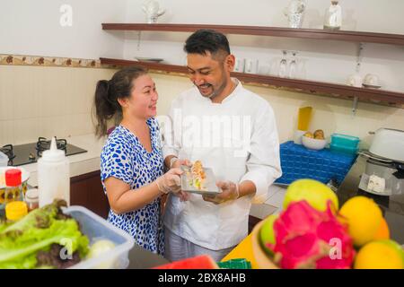 happy Asian couple cooking together -  home kitchen lifestyle portrait of Chinese cheerful and sweet husband and wife making delicious traditional Jap Stock Photo