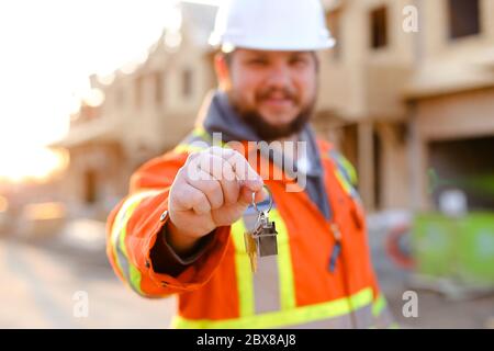 Focus on keys from new home given by foreman in helmet. Stock Photo