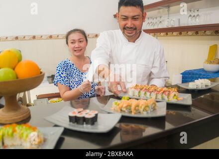 happy Asian couple cooking together -  home kitchen lifestyle portrait of Chinese cheerful and sweet husband and wife making delicious traditional Jap Stock Photo