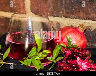 Still life of a red, pomegranate flavored gin and tonic cocktail, pomegranate fruit and leaves, against a brick Background Stock Photo