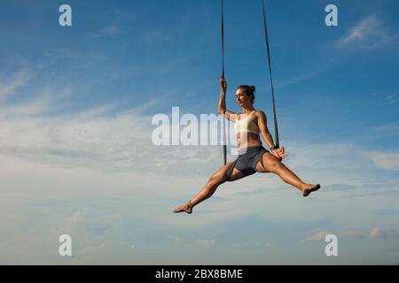 aerial yoga meditation workout  isolated on blue sky - young attractive and healthy woman practicing aero-yoga training balance body and mind control Stock Photo