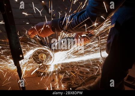 Side view of a man's hands working on a metal part of a garden bench, using an electric grinder while sparks are flying around in the industrial works Stock Photo