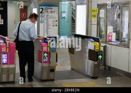 Passenger uses IC card ticket gate at Tozai Line station. People wear face masks & a plastic shield covers the ticket gate window due to  coronavirus. Stock Photo