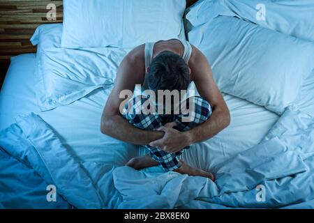 dramatic lifestyle portrait of young attractive sad and depressed man sitting on bed awake at night feeling stressed and desperate suffering depressio Stock Photo