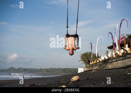 outdoors portrait of  man practicing aero yoga workout at the beach hanging from rope swing above the sea training body balance and flexibility in hea Stock Photo