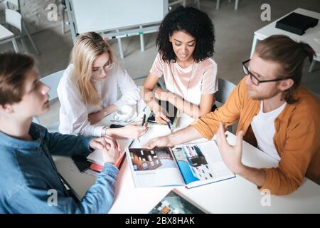 Portrait of young people sitting in office discussing something. Group of cool guys working on new project while sitting at cafe. Young students study Stock Photo