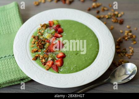 Green smoothie bowl with banana, strawberry, spinach, kale, kiwi, coconut milk garnished with homemade oat, nut and seed granola, coconut flakes, chia Stock Photo