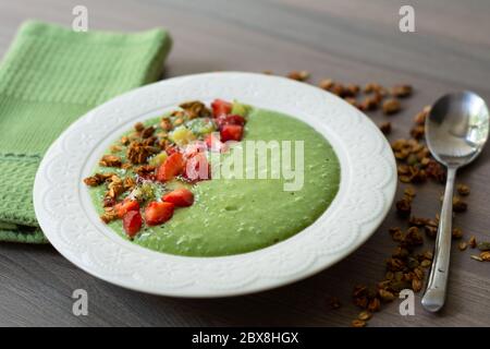 Green smoothie bowl with banana, strawberry, spinach, kale, kiwi, coconut milk garnished with homemade oat, nut and seed granola, coconut flakes, chia Stock Photo
