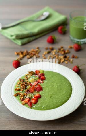 Green smoothie bowl with banana, strawberry, spinach, kale, kiwi, coconut milk garnished with homemade oat, nut and seed granola, coconut flakes, chia Stock Photo