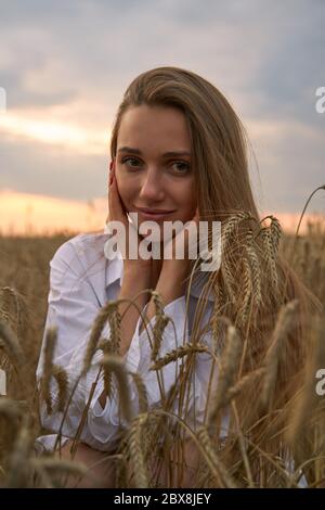Happy smiling blonde girl is wearing white fashion dress with long hair in field of ray. Stock Photo