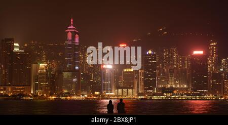 Silhouette of a couple of lovers in front of Victoria harbour skyline in Hong Kong island at night from West Kowloon park - Hong Kong Stock Photo