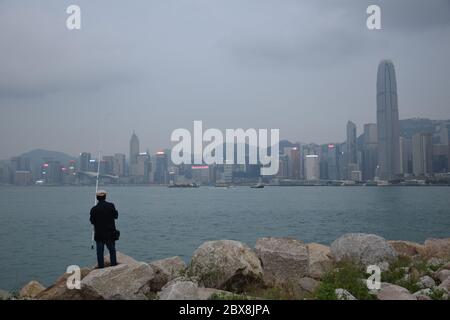 Local man fishing in West Kowloon park in front of Victoria harbour in Hong Kong island - Hong Kong Stock Photo