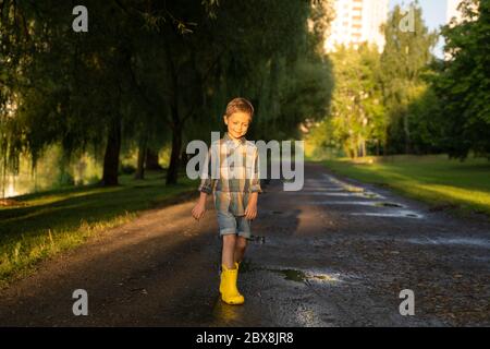 Preschooler child wearing yellow rain boots walking in park after rain. Kid playing and having fun in sunny spring or summer day. Outdoors games for Stock Photo