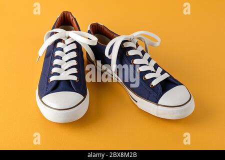 Pair of blue sneakers or gumshoes with white shoe laces on a textured bright yellow background. Comfortable shoes for fitness and sport. Front view. Stock Photo