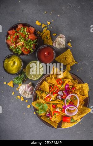 Nachos chips with melted cheese and various traditional mexican dips, salsa and jalapeno, dark grey background top view copy space Stock Photo