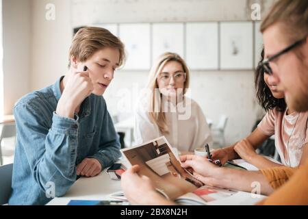 Portrait of young people thoughtfully looking at photo in journal. Group of cool guys working on new project in office. Young students creating someth Stock Photo