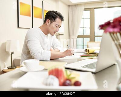 young asian man design professional sitting at kitchen counter working from home (artwork in background digitally altered) Stock Photo