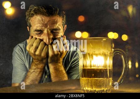 young desperate and depressed alcoholic man drinking beer wasted and drunk failing resisting to drink in bar pub at night falling into alcohol abuse i Stock Photo