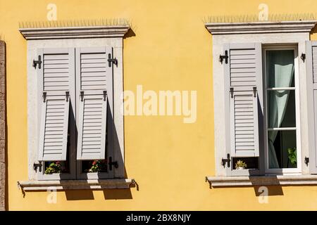Two windows with grey wooden shutters with spike steel sticks to prevent birds from stopping, especially pigeons, residential building in Italy. Stock Photo