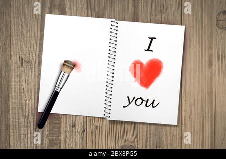 notebook opened on old vintage wooden table with I love you handwritten and red heart shape painted with makeup paintbrush as message celebrating roma Stock Photo