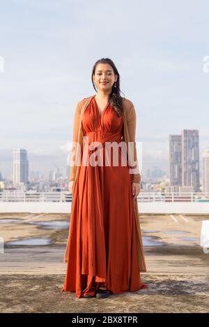 Full body shot of happy young beautiful Indian woman smiling against view of the city Stock Photo