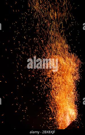 Flame of fire with flying burning red sparks on a black background. Fiery orange glowing particles flying away in night sky. Closeup of beautiful flam Stock Photo