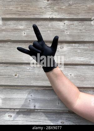 Hand with black rubber protect glove gesturing rock, rocker, goat, roxanne. Signs of gestures language, gloves cleaning, kitchen or medical gloves. Stock Photo