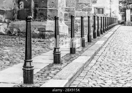 Row of iron pillars between cobbled street and pedestrian sidewalks. Black and white image. Stock Photo