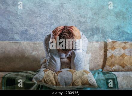 young sad and desperate man at home sitting at living sofa couch holding head with hands suffering depression and stress about problem crying in frust Stock Photo
