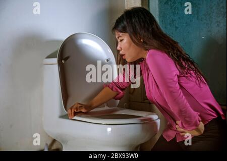 young drunk or pregnant Asian woman vomiting and throwing up in toilet WC feeling unwell and sick suffering stomach ache and nausea as pregnancy sympt Stock Photo