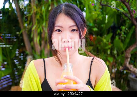 young attractive and happy Asian Korean girl having fun in garden outdoors drinking healthy orange juice with straw playful having fun in carefree wom Stock Photo