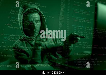 computer programmer man in hoodie hacking system entering code pointing to laptop hacking and decoding system data illegal access breaking password on Stock Photo