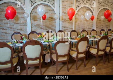 A festive table with a white tablecloth served . Red an white balloons are tied to chairs. Preparing for a children's birthday . White and red, with Stock Photo