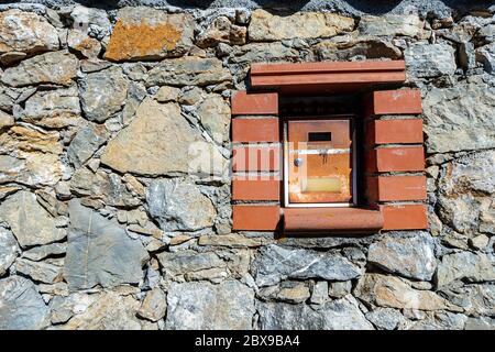 Close-up of an old and rusty metal mailbox embedded in the stone wall. Liguria, Italy Stock Photo