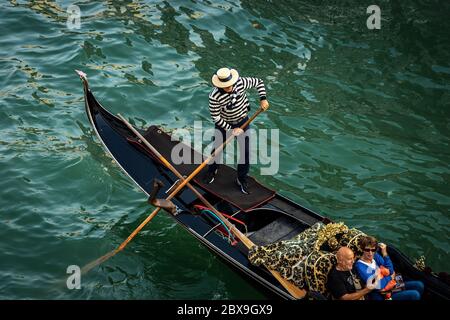 Two tourists sitting in the gondola with a gondolier, typical Venetian rowing boat. Sightseeing tour along the Grand Canal of the famous city Stock Photo