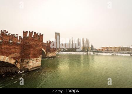 Verona. Ponte Scaligero (medieval bridge) and Castelvecchio (Old Castle) with the River Adige in winter while it snows. UNESCO world heritage site. Stock Photo
