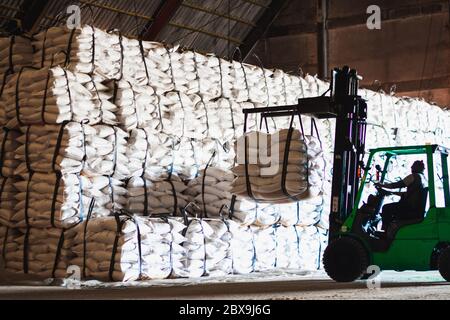 Forklift carries jumbo bag of refine white sugar to put on the stack inside warehouse. Sugar warehouse operations and management. Stock Photo