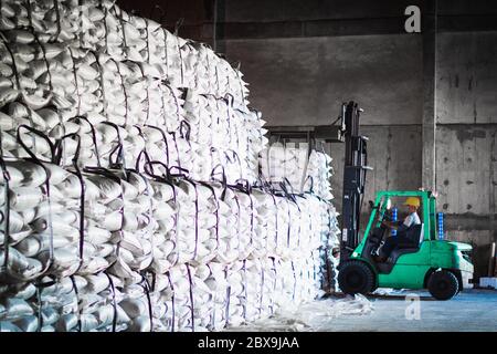 Forklift carries jumbo bag of refine white sugar to put on the stack inside warehouse. Sugar warehouse operations and management. Stock Photo