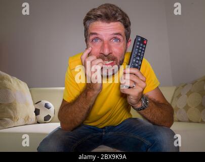 close up expressive portrait of young excited and nervous football supporter man watching soccer game on television at living room sofa feeling crazy Stock Photo