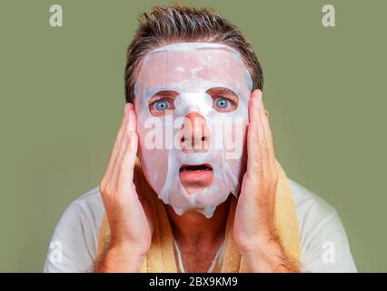 lifestyle isolated background portrait of young weird and funny man at home trying using beauty paper facial mask cleansing learning anti aging treatm Stock Photo