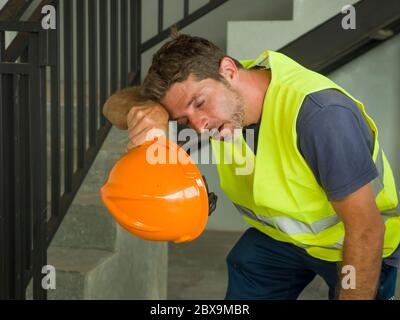 blue collar job lifestyle. Portrait of attractive and exhausted construction worker in helmet and vest at building site taking a breath during a hard Stock Photo