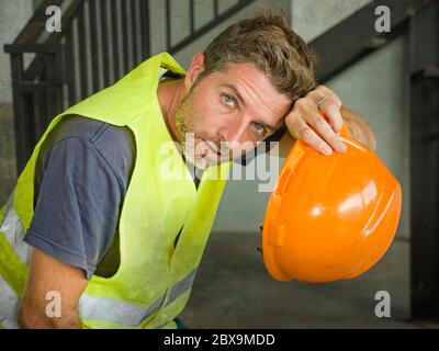 blue collar job lifestyle. Portrait of attractive and exhausted construction worker in helmet and vest at building site taking a breath during a hard Stock Photo